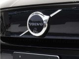 【ボルボの電気自動車を象徴するフロントフェイス】時代に合わせて変化するエンブレムデザイン。センターを斜めに大きく横切るラインと黒地に銀のアイアンマーク、これが最新ボルボのキャラクターアイコンです。