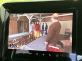 画面にはテレビ番組が表示され、映像を楽しめるエンターテインメント環境です。下部には音量や再生に関する操作アイコンが並び、画面を見ながら扱いやすい配置となっています。